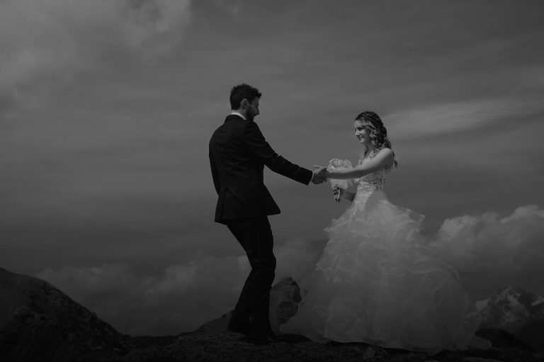 Gli sposi si tengono per mano durante una danza spontanea in alta quota, con il vento che muove l’abito della sposa e il cielo come sfondo.